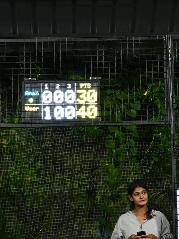 A Tovio board lit above a court while someone scores the match from their phone below it