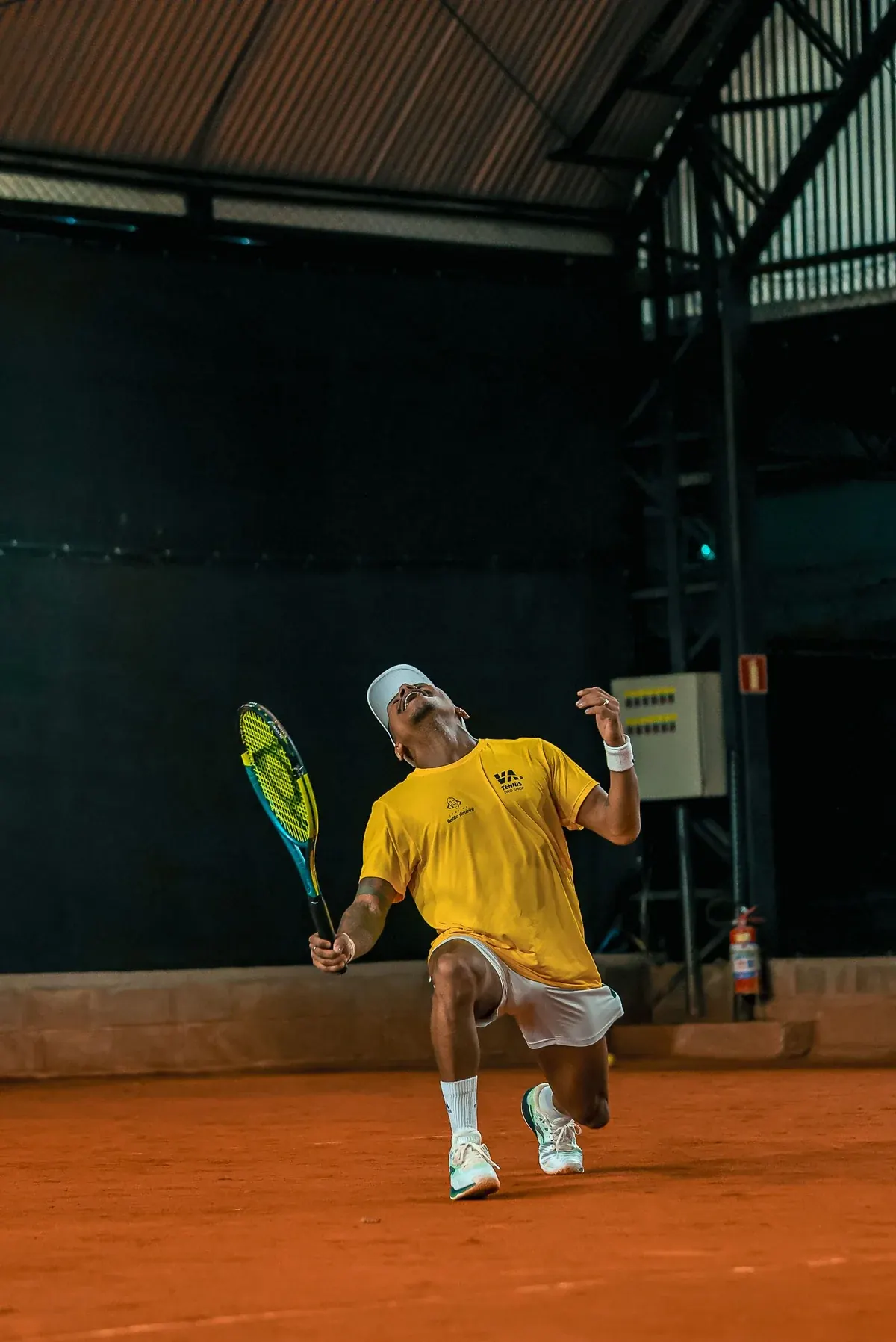 A player reaching up to serve on a floodlit clay court