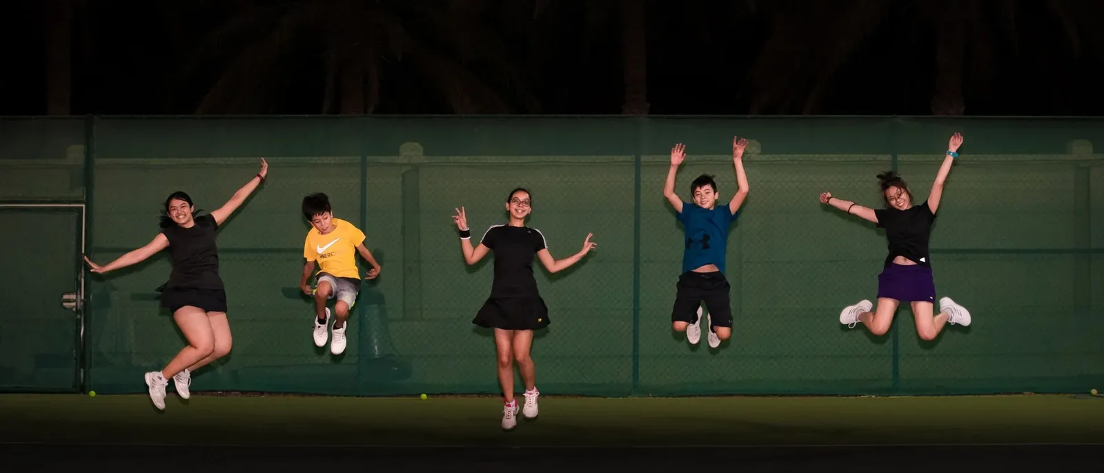 Junior players leaping in celebration on a floodlit court at night