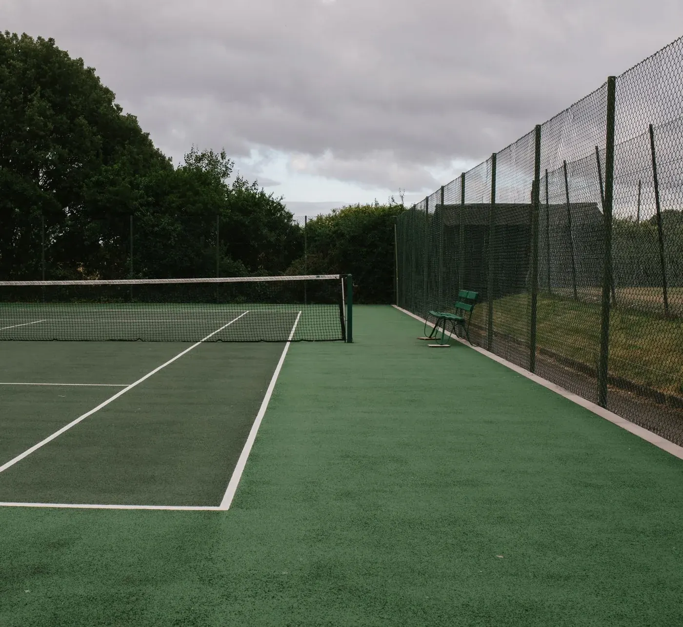 A deserted court under a grey sky, the net still up and nobody on it