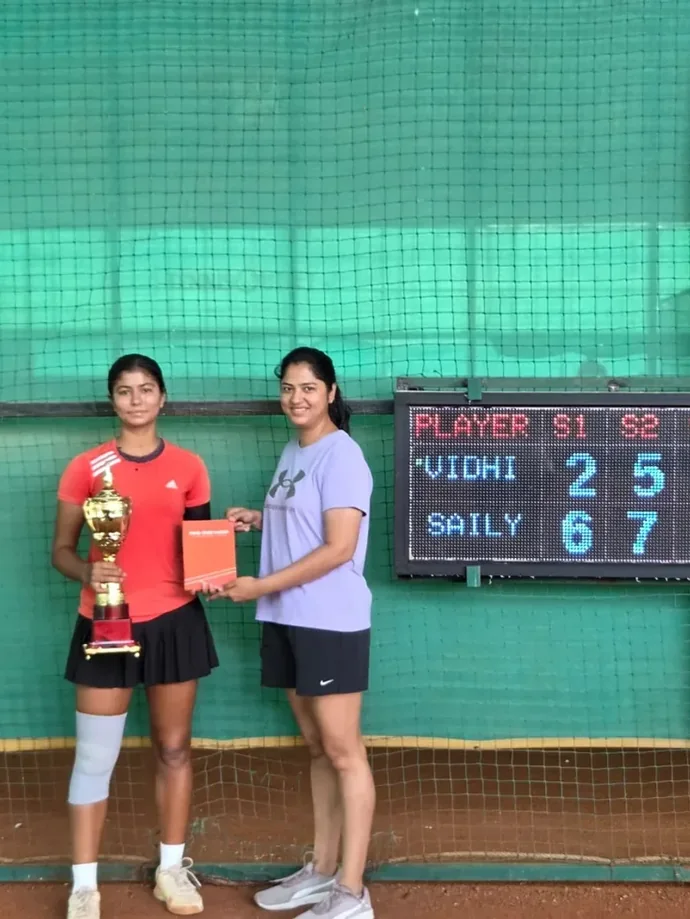 A player with her trophy and the Tovio journal, the board behind her showing the set scores